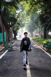 Portrait of young man standing on road against trees