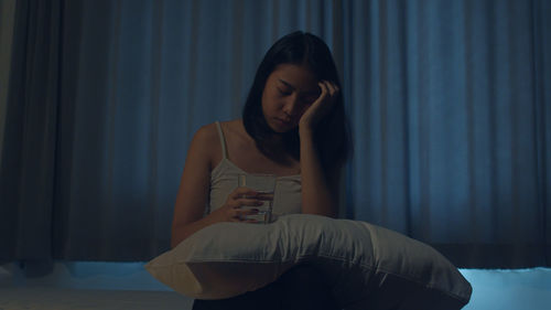 Young woman sitting against wall at home