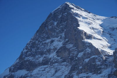 Low angle view of snowcapped mountain against clear blue sky