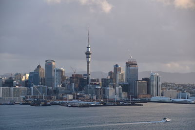 Sky tower in city by river against cloudy sky