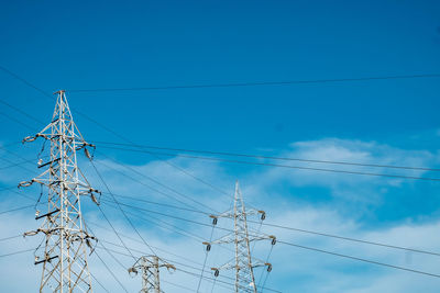 Low angle view of electricity pylon against blue sky