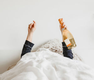 Person in bed, covered with white linen, holding champagne bottle and glass.