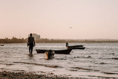 People on sea against clear sky during sunset