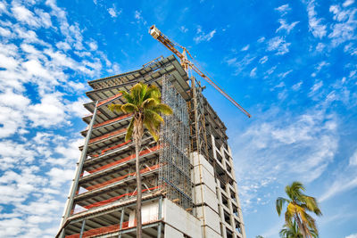 Low angle view of crane by building against sky