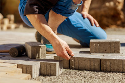 Young man laying gray concrete paving slabs in house courtyard on gravel foundation base. 