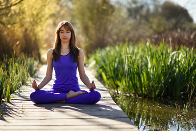 Full length of woman doing yoga on boardwalk against plants