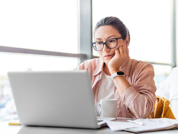 Frowned woman in eyeglasses works with laptop. co-working workplace for freelancers or students.