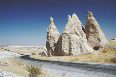 Rock formations on road against clear blue sky