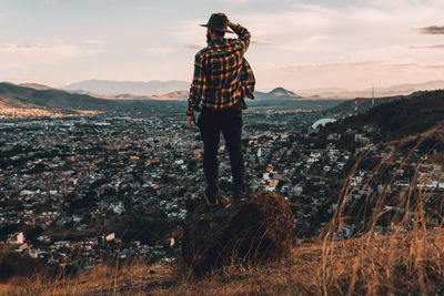 Male on rock posing in vintage clothes on golden hilltop overlooking a valley at sunset.