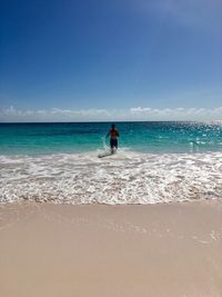 Rear view of man walking in sea against blue sky during sunny day