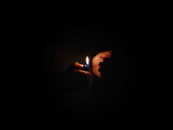 Person hand holding lit candle in darkroom