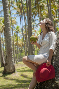 Side view of young woman sitting on tree