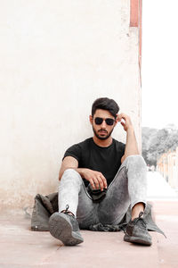 Portrait of young man sitting against wall