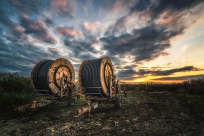 Pipe spools on field against sky during sunset