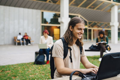 Young woman using mobile phone while sitting on laptop