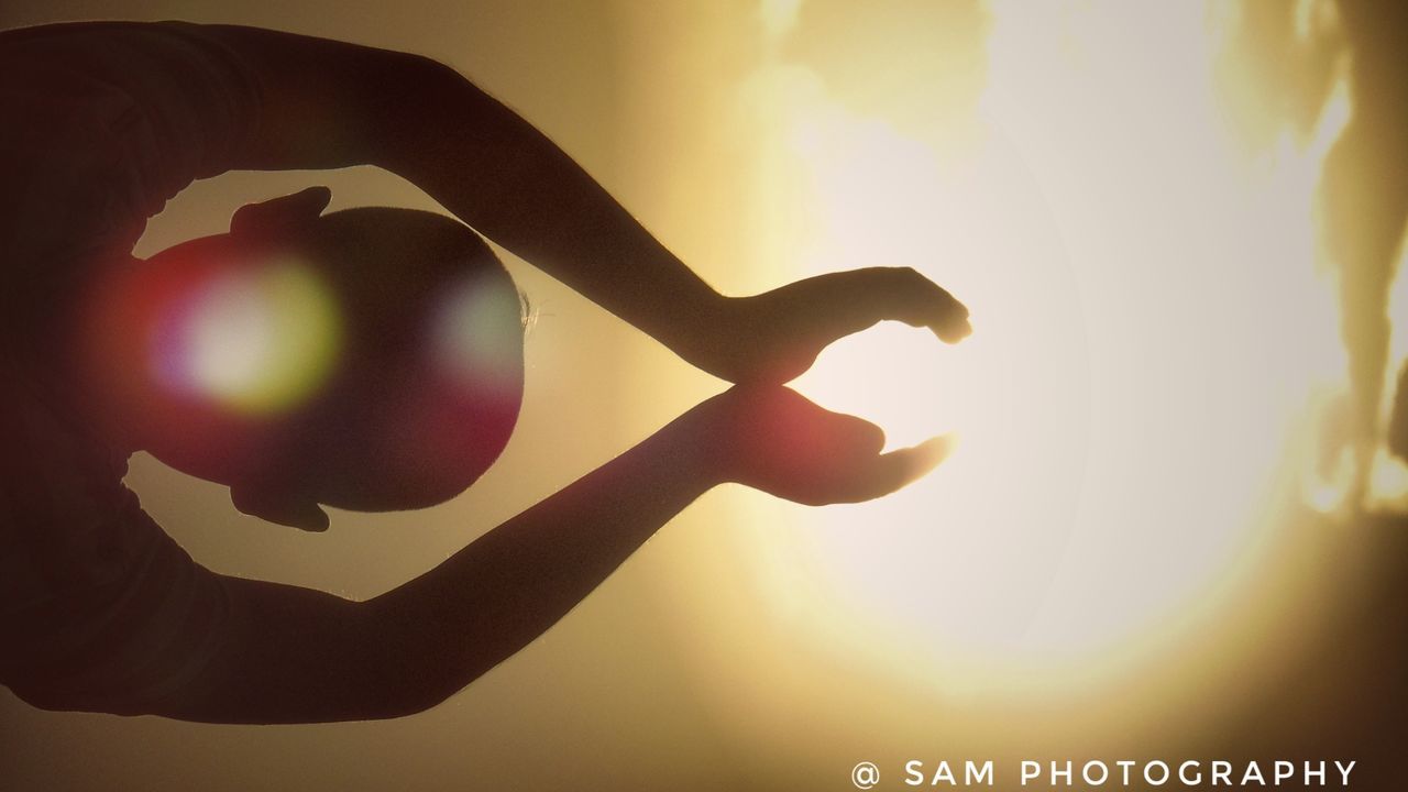 CLOSE-UP OF HAND AGAINST ILLUMINATED SKY