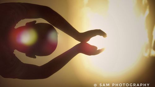 Close-up of silhouette hand against illuminated sky