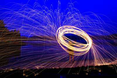 Person spinning wire wool by lake against sky at night