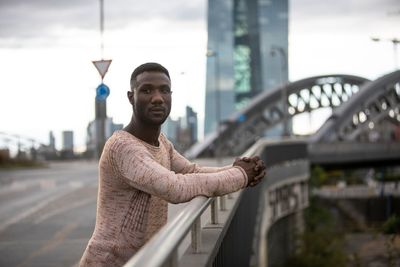 Young man looking away standing against city