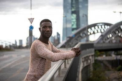 Portrait of young man standing against bridge in city