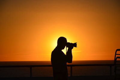 Silhouette man photographing against sky during sunset