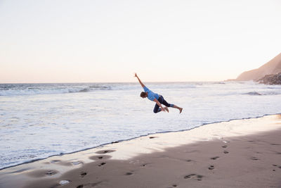 Man jumping on beach against clear sky