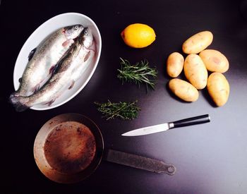 High angle view of fish by potatoes and frying pan on table