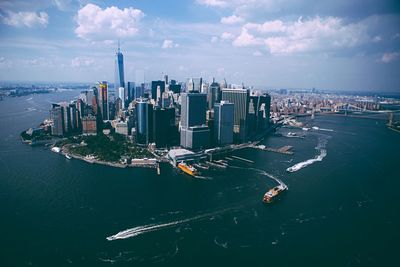 One world trade center amidst modern buildings amidst sea against cloudy sky