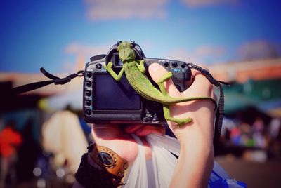 Close-up of woman hand holding camera against sky