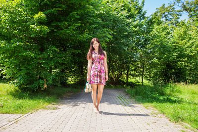 Full length portrait of young woman standing against trees