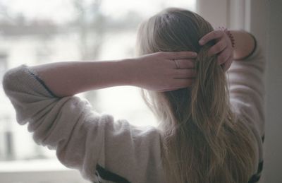 Rear view of woman with hand in hair standing at home