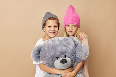 Portrait of sibling holding stuffed toy against beige background