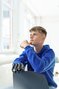 Thoughtful teenage boy with amputated arm sitting on chair