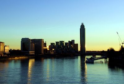 Scenic view of river by buildings against sky during sunset