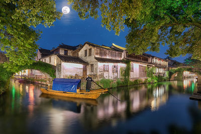 Man sailing in lake against building at dusk