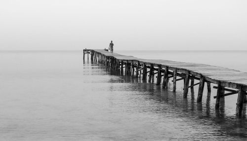 Man walking on pier over sea against clear sky