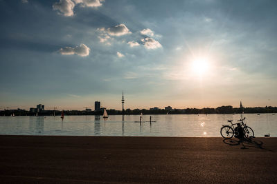 Silhouette bicycle on beach against sky during sunset