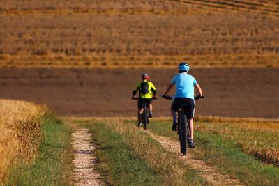 Rear view of men riding bicycle on field