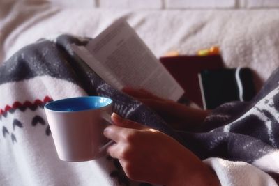 Close-up of hand holding coffee cup on bed