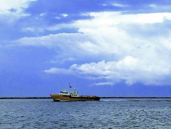 Boat sailing in sea against cloudy sky