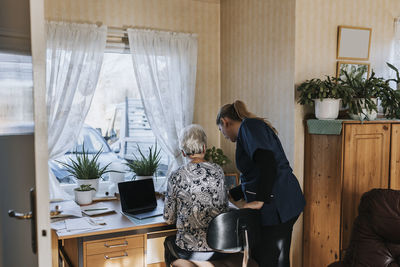 Home caretaker helping senior woman use laptop