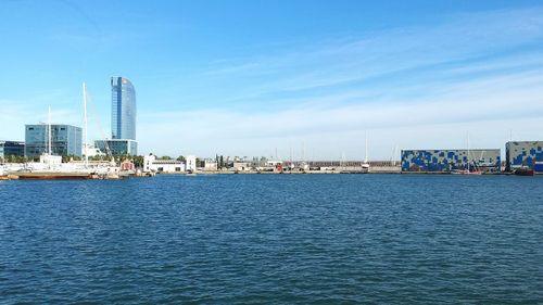 Sea by modern buildings against blue sky