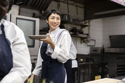 Smiling chef carrying plate while walking in restaurant kitchen