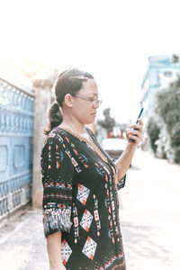 Side view of woman using phone while standing on road