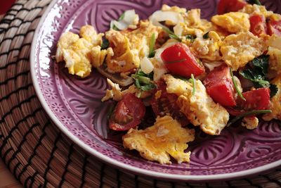 High angle view of scrambled eggs with tomatoes in plate on mat