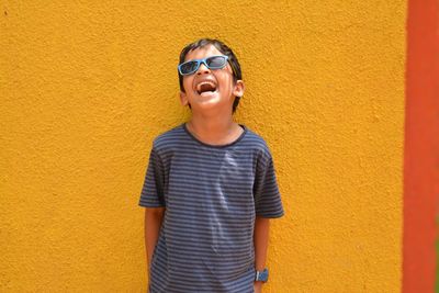 Happy boy laughing against yellow wall