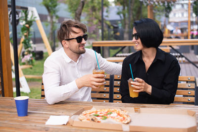 A guy and a girl are holding cocktails with a straw in their hands and eating pizza