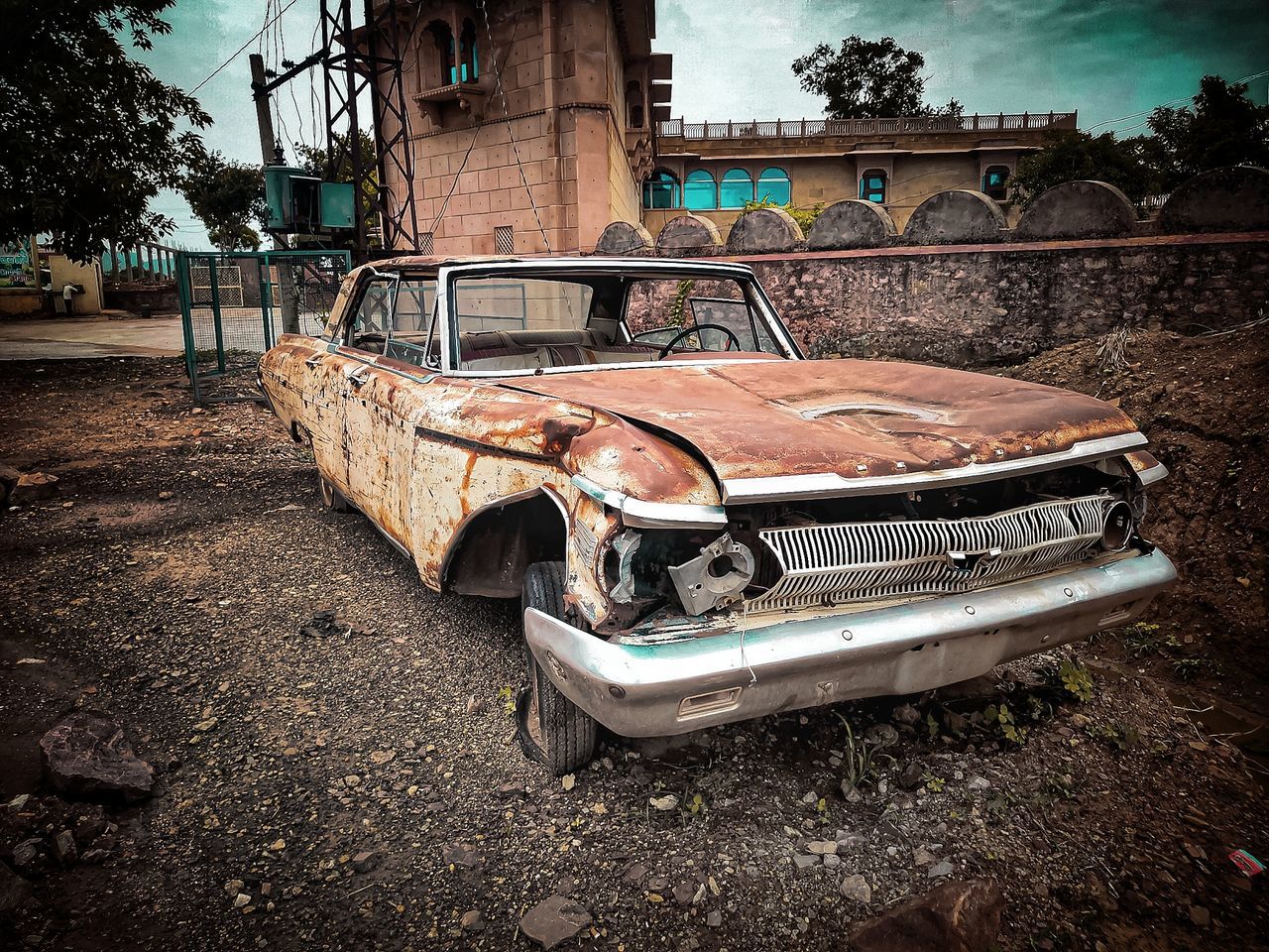car, mode of transportation, motor vehicle, transportation, vintage car, vehicle, architecture, abandoned, land vehicle, built structure, damaged, retro styled, tree, old, no people, building exterior, nature, day, sky, automobile, plant, history, rundown, antique car, city, the past, outdoors, metal, street, rusty, cloud