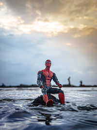 Full length of man with arms raised in sea against sky