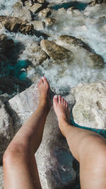 Low section of woman sitting on rock amidst river